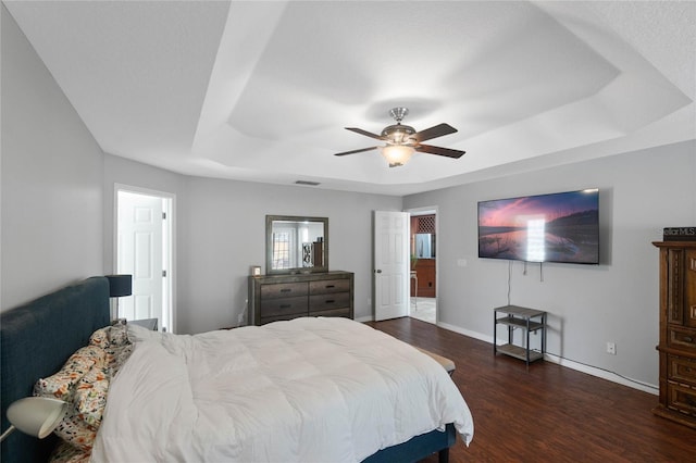 bedroom with dark hardwood / wood-style floors, ceiling fan, and a tray ceiling