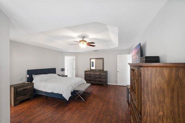 bedroom with ceiling fan, a tray ceiling, and dark hardwood / wood-style flooring