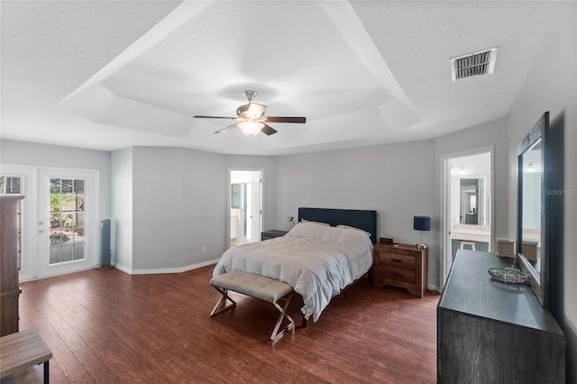 bedroom featuring access to exterior, ceiling fan, a raised ceiling, dark wood-type flooring, and ensuite bath