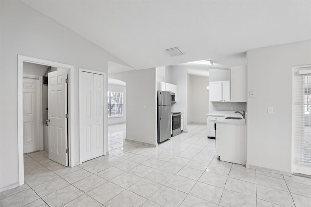 kitchen featuring sink, vaulted ceiling, light tile patterned floors, white cabinetry, and stainless steel appliances