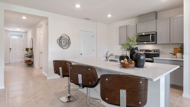 kitchen with gray cabinets, appliances with stainless steel finishes, an island with sink, and light tile patterned flooring