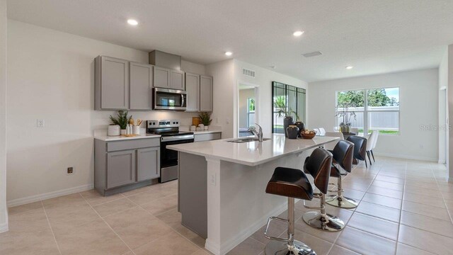 kitchen featuring sink, a breakfast bar, appliances with stainless steel finishes, a kitchen island with sink, and gray cabinetry