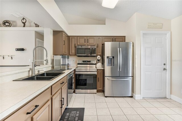 kitchen with stainless steel appliances, vaulted ceiling, a textured ceiling, sink, and light tile patterned floors