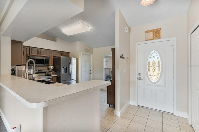 kitchen with stainless steel appliances, a textured ceiling, light tile patterned floors, kitchen peninsula, and lofted ceiling