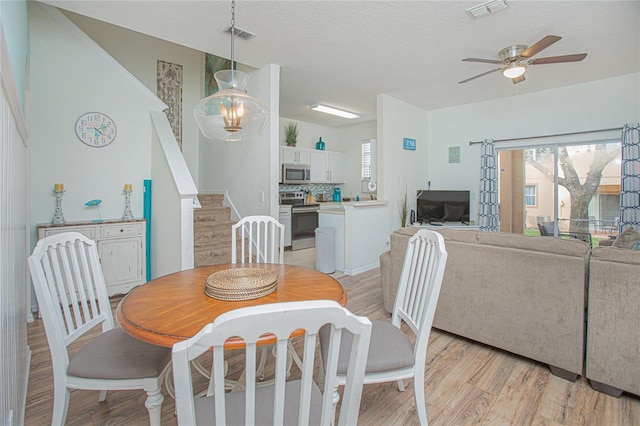 dining space featuring ceiling fan with notable chandelier, a textured ceiling, and light hardwood / wood-style floors