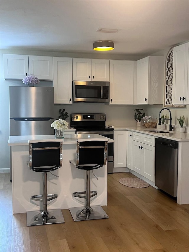 kitchen featuring white cabinetry, light wood-type flooring, appliances with stainless steel finishes, and a breakfast bar area