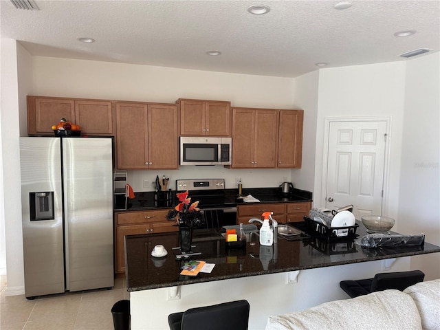 kitchen with a kitchen bar, light tile patterned floors, an island with sink, and appliances with stainless steel finishes