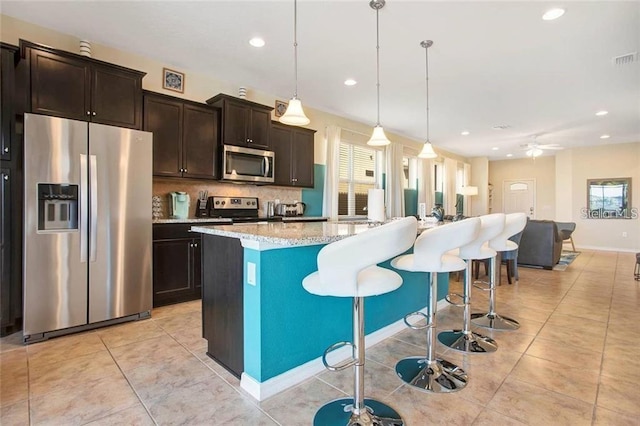 kitchen featuring stainless steel appliances, dark brown cabinets, pendant lighting, ceiling fan, and a kitchen island with sink