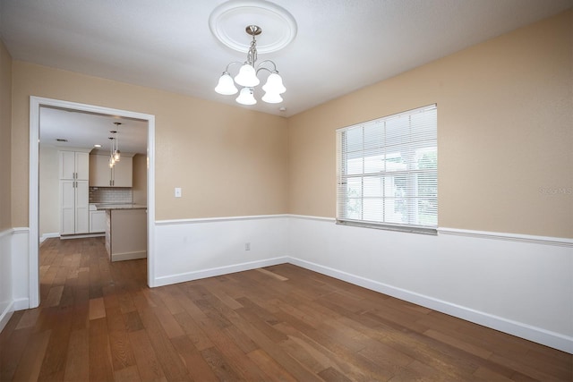 unfurnished room featuring dark wood-type flooring and a notable chandelier