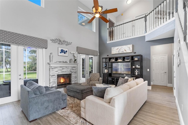 living room featuring ceiling fan, high vaulted ceiling, a stone fireplace, light wood-type flooring, and french doors