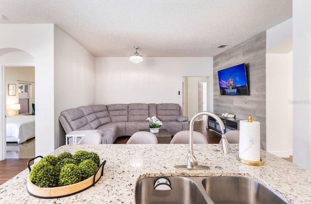 kitchen featuring hardwood / wood-style flooring, sink, light stone counters, and a textured ceiling