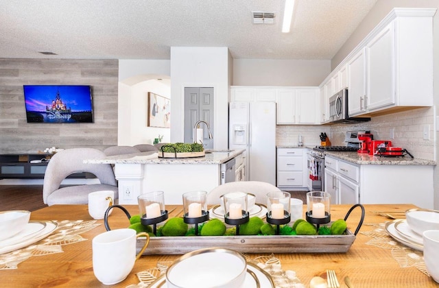 kitchen with white cabinetry, light stone counters, appliances with stainless steel finishes, a textured ceiling, and backsplash