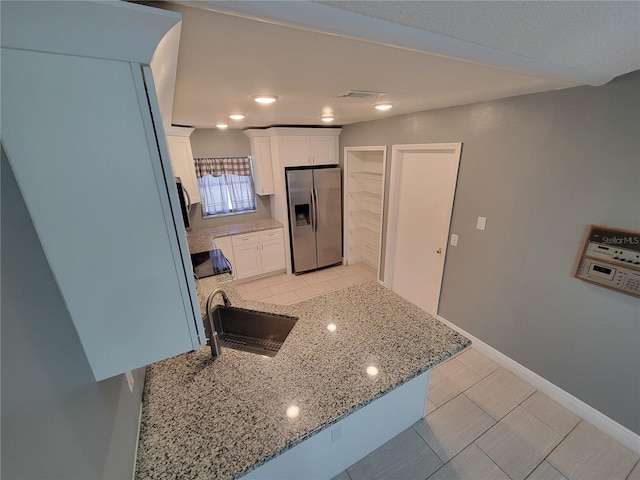 kitchen featuring light stone countertops, sink, light tile patterned floors, stainless steel fridge with ice dispenser, and white cabinets