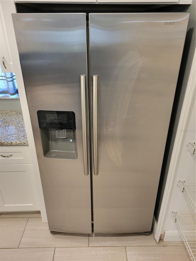 interior details featuring light stone countertops, white cabinets, and stainless steel refrigerator with ice dispenser