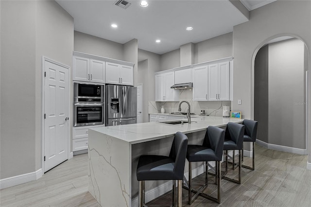 kitchen featuring white cabinets, stainless steel refrigerator with ice dispenser, built in microwave, a breakfast bar, and light stone countertops