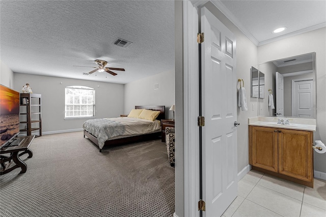 bedroom featuring ceiling fan, a textured ceiling, crown molding, light colored carpet, and connected bathroom