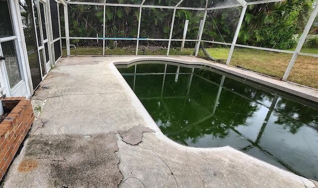 view of pool featuring glass enclosure, a lawn, and a patio area