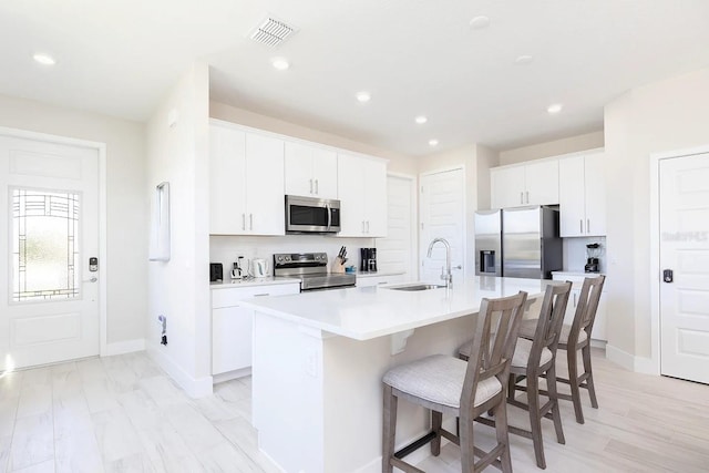 kitchen featuring appliances with stainless steel finishes, sink, an island with sink, white cabinets, and light hardwood / wood-style flooring