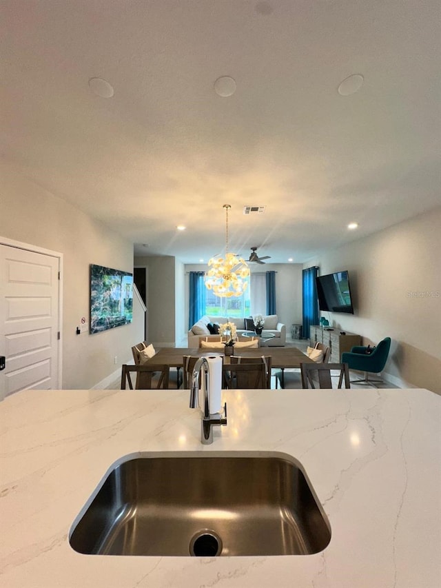 kitchen featuring light stone countertops, ceiling fan with notable chandelier, sink, and pendant lighting