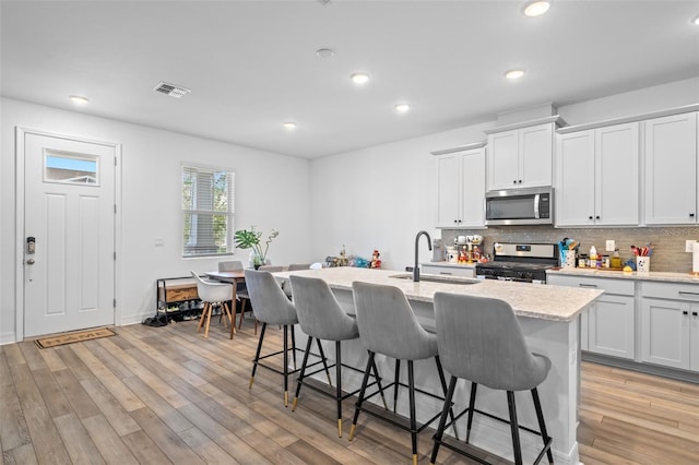 kitchen featuring a kitchen bar, a center island with sink, sink, light wood-type flooring, and appliances with stainless steel finishes