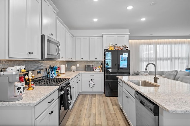 kitchen with white cabinetry, sink, appliances with stainless steel finishes, a kitchen island with sink, and light hardwood / wood-style flooring