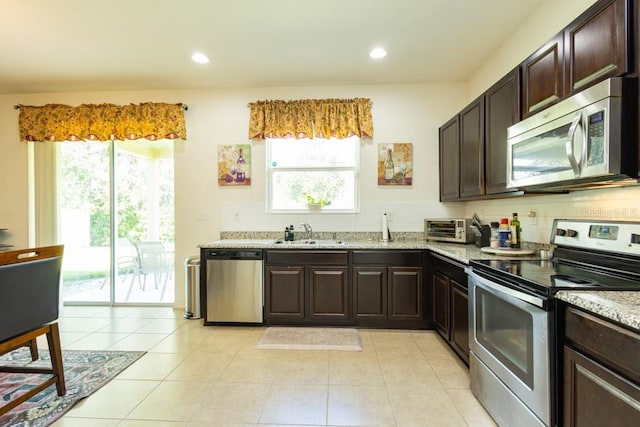 kitchen featuring stainless steel appliances, dark brown cabinetry, sink, light stone countertops, and light tile patterned floors