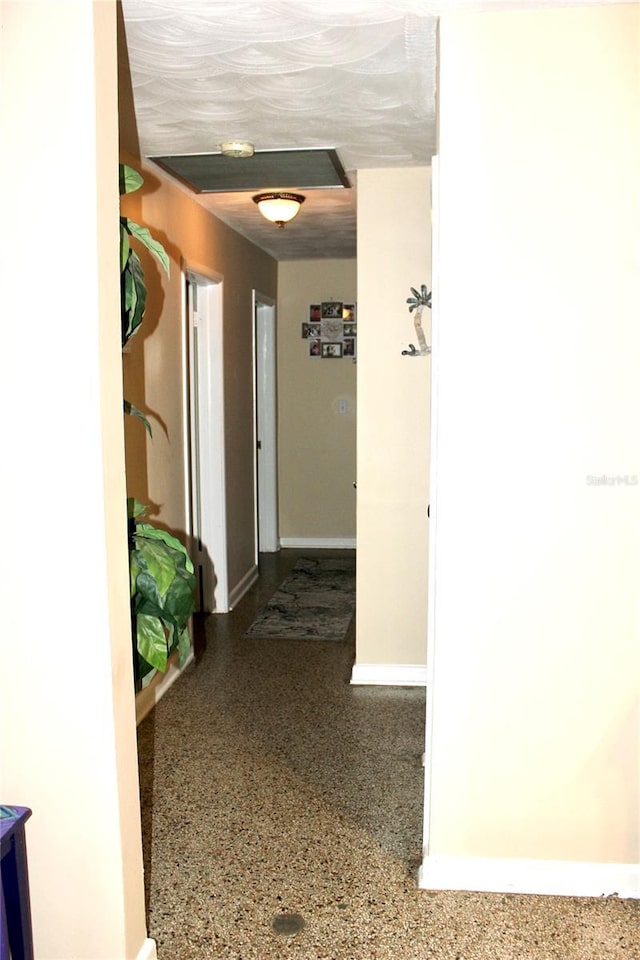 hall featuring speckled floor and baseboards