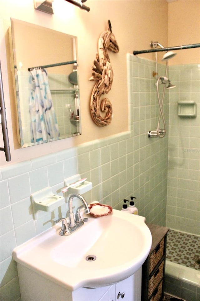 full bathroom with a tile shower, tile walls, a sink, and a wainscoted wall