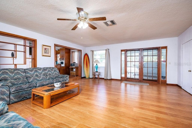 living room featuring ceiling fan, a textured ceiling, and light hardwood / wood-style flooring