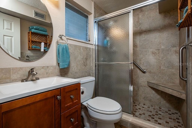 bathroom featuring walk in shower, a textured ceiling, vanity, toilet, and tile walls