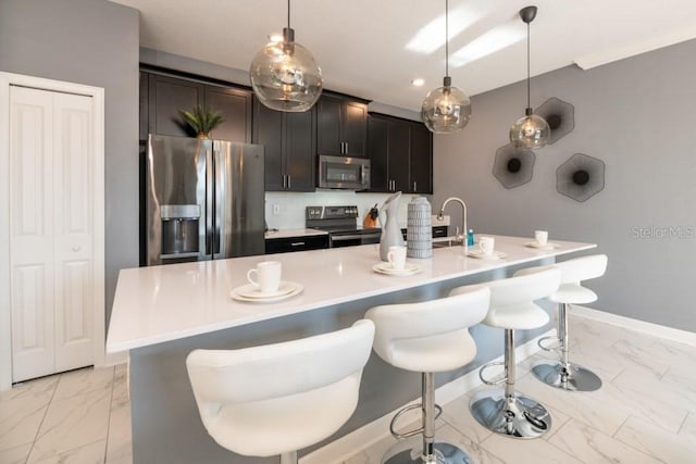 kitchen featuring pendant lighting, stainless steel appliances, a center island with sink, and a breakfast bar area