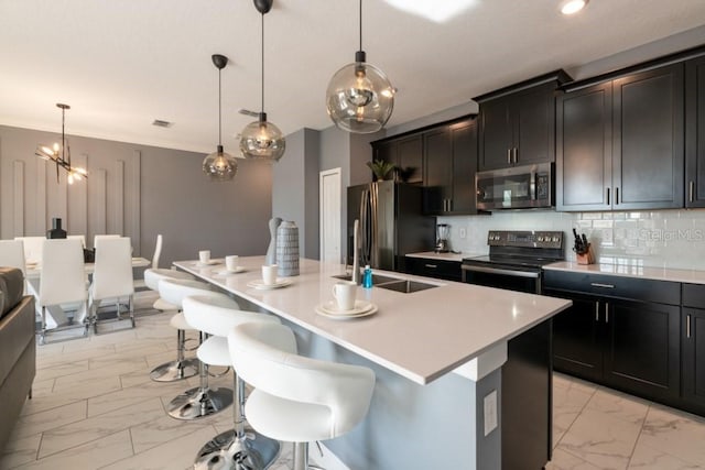 kitchen with stainless steel appliances, decorative backsplash, hanging light fixtures, a breakfast bar area, and an island with sink