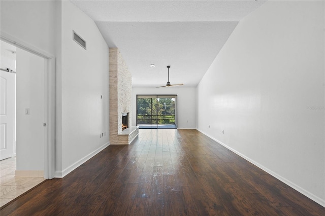 unfurnished living room with a stone fireplace, a textured ceiling, hardwood / wood-style floors, vaulted ceiling, and ceiling fan