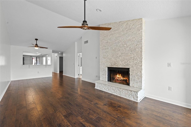 unfurnished living room featuring a stone fireplace, dark hardwood / wood-style flooring, a textured ceiling, and ceiling fan