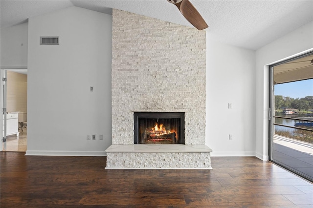 unfurnished living room featuring a water view, a textured ceiling, a stone fireplace, dark wood-type flooring, and vaulted ceiling