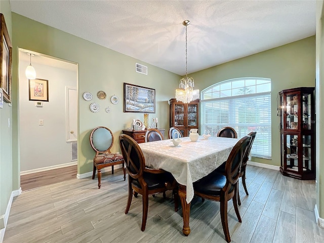 dining room featuring light wood-type flooring, a textured ceiling, and a notable chandelier