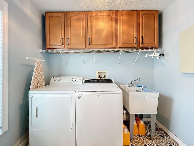 clothes washing area with cabinets, washing machine and dryer, a textured ceiling, and sink