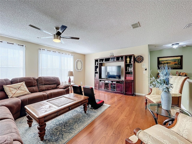 living room with a textured ceiling, ceiling fan, and light hardwood / wood-style flooring