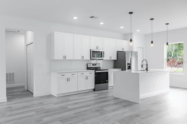 kitchen with a center island with sink, hanging light fixtures, white cabinetry, light wood-type flooring, and appliances with stainless steel finishes