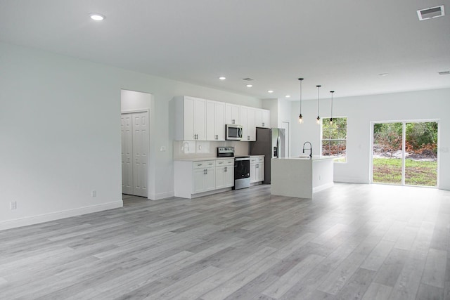 kitchen with stainless steel appliances, a center island with sink, white cabinetry, light hardwood / wood-style flooring, and decorative light fixtures