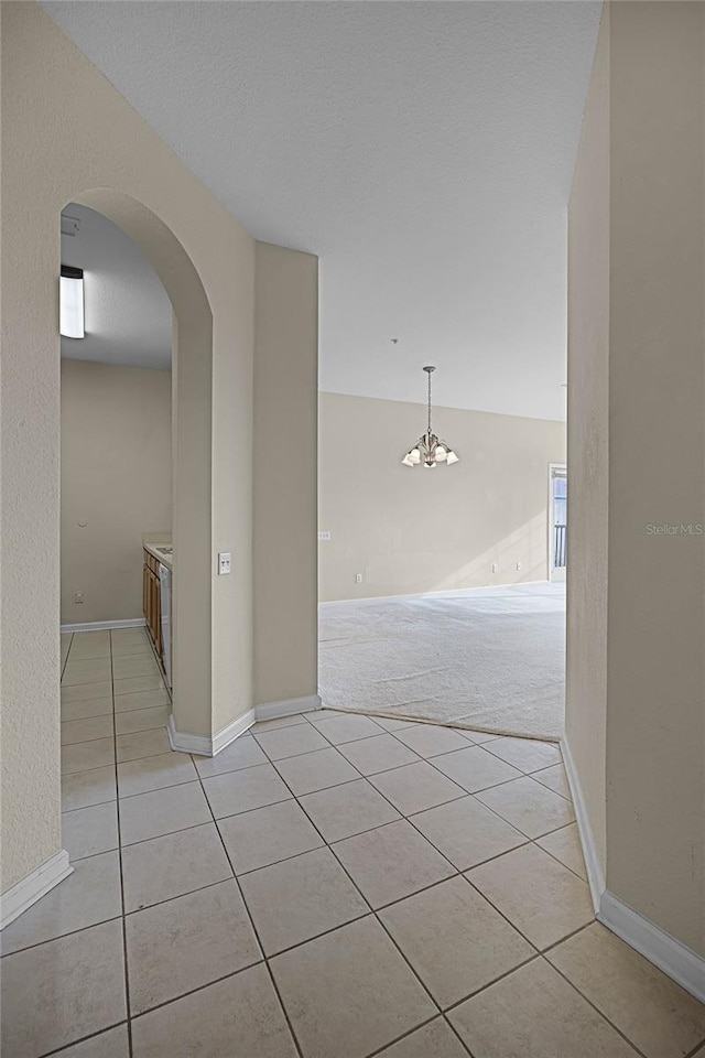 corridor with an inviting chandelier, light colored carpet, and a textured ceiling