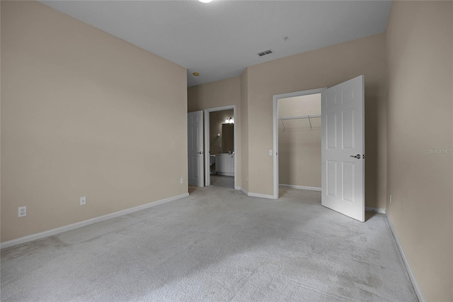 unfurnished bedroom with a walk in closet, ensuite bath, a closet, and light colored carpet