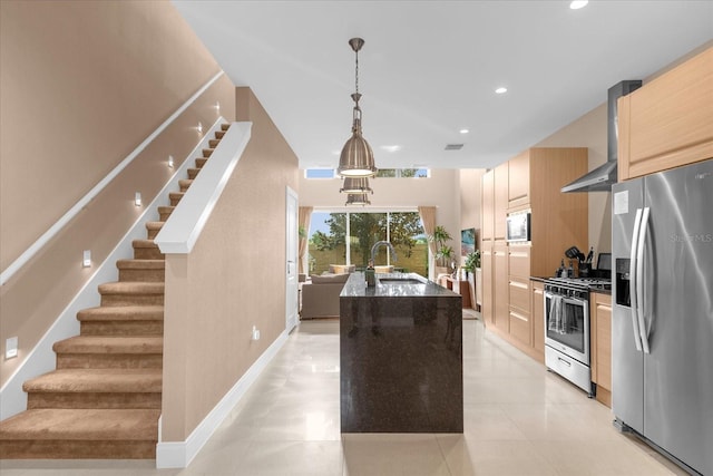 kitchen featuring sink, hanging light fixtures, stainless steel appliances, wall chimney range hood, and a kitchen island with sink