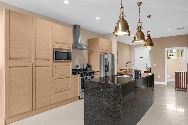 kitchen with stainless steel appliances, sink, wall chimney range hood, decorative light fixtures, and a center island with sink