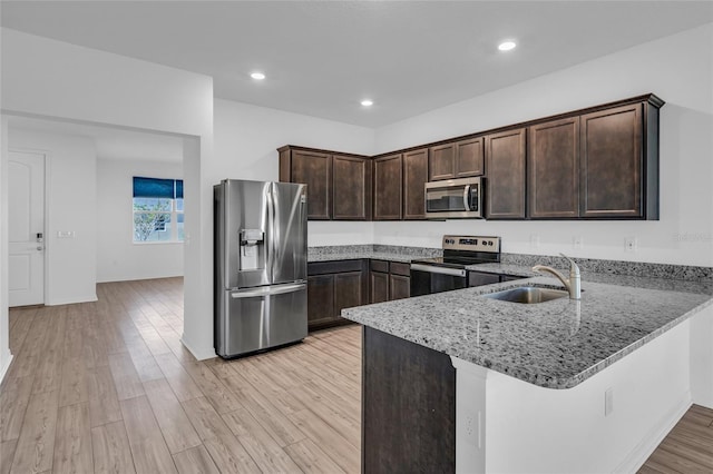 kitchen featuring appliances with stainless steel finishes, sink, kitchen peninsula, light stone countertops, and light hardwood / wood-style flooring