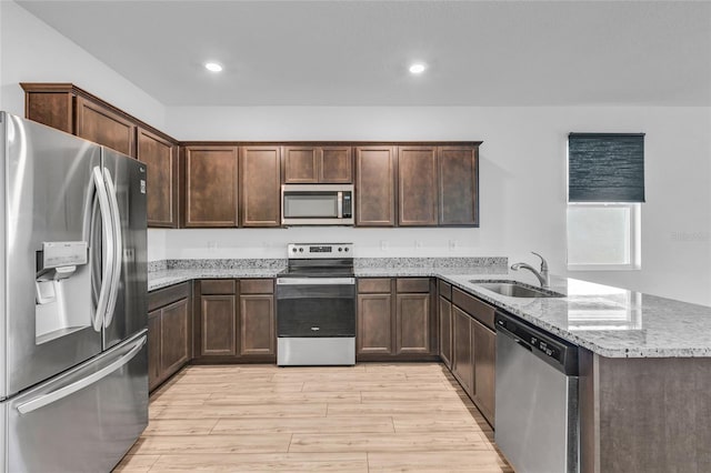 kitchen with appliances with stainless steel finishes, sink, light stone counters, kitchen peninsula, and light hardwood / wood-style flooring