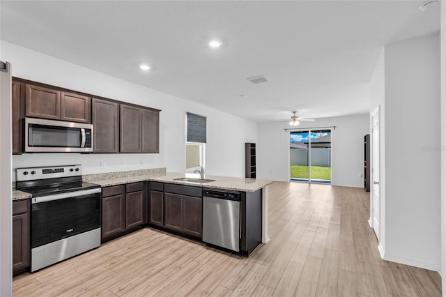 kitchen featuring stainless steel appliances, sink, light stone counters, and light wood-type flooring