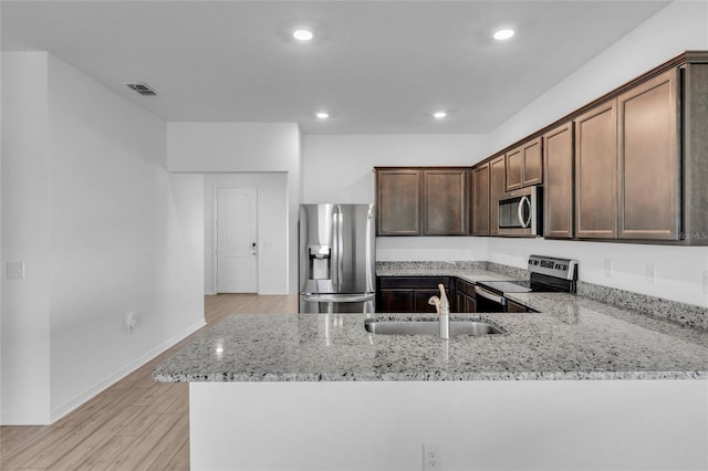 kitchen featuring sink, light stone counters, kitchen peninsula, stainless steel appliances, and light hardwood / wood-style flooring