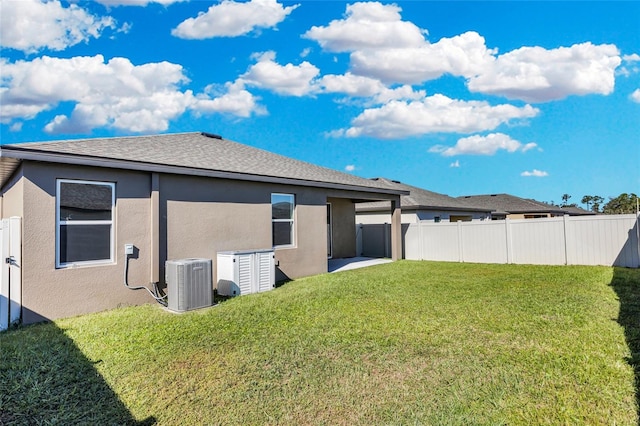 rear view of house with central AC and a lawn