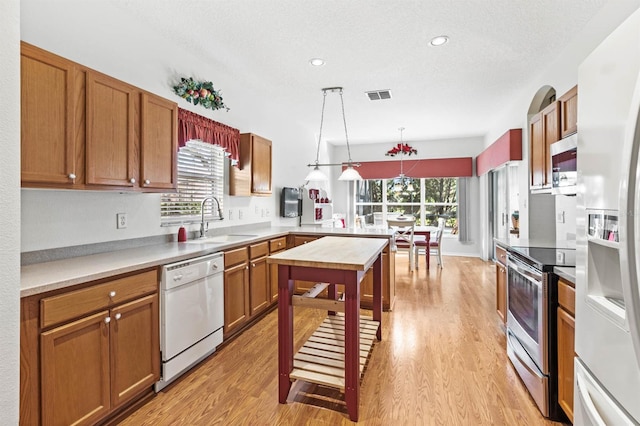 kitchen with pendant lighting, sink, light wood-type flooring, a textured ceiling, and stainless steel appliances